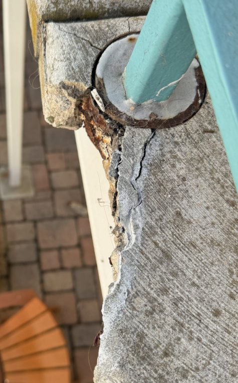 Broken concrete edge around a railing post before repair