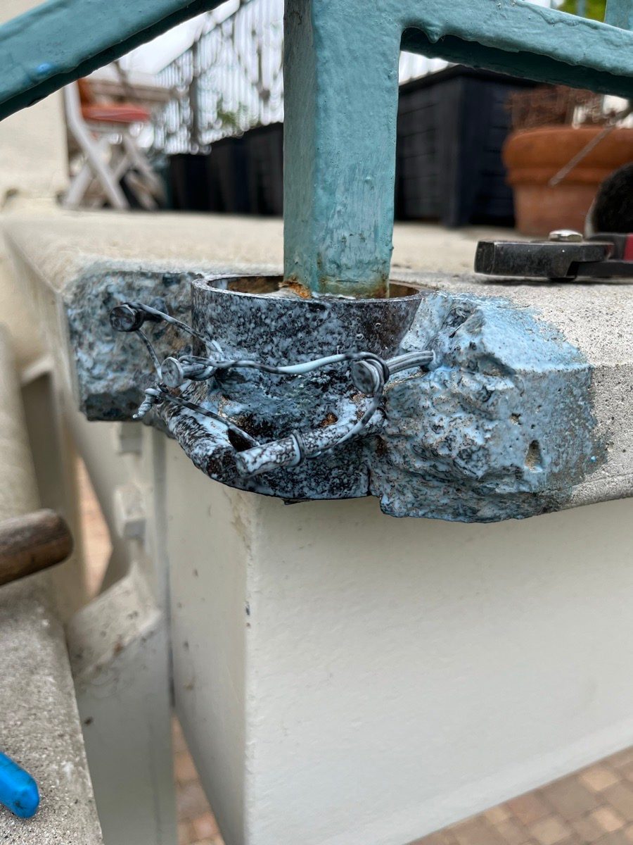 Damaged concrete corner around a blue railing post before repair