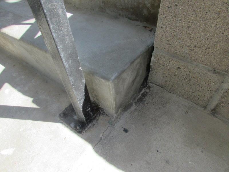 Rebuilt concrete stair corner near a black railing post after repair