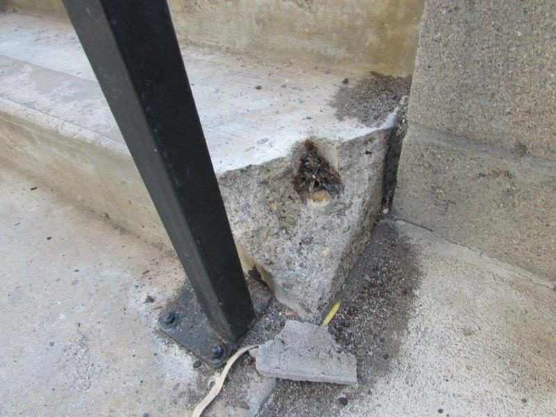 Broken concrete stair corner near a black railing post before repair